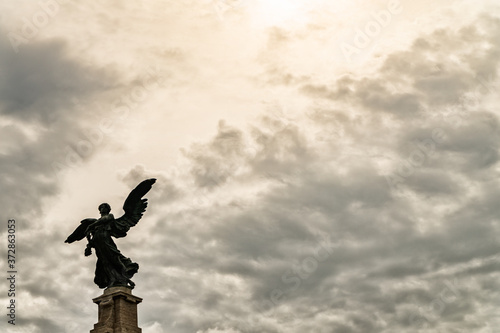 Statue of an angel in Rome and clouds background with sun rays as divine light