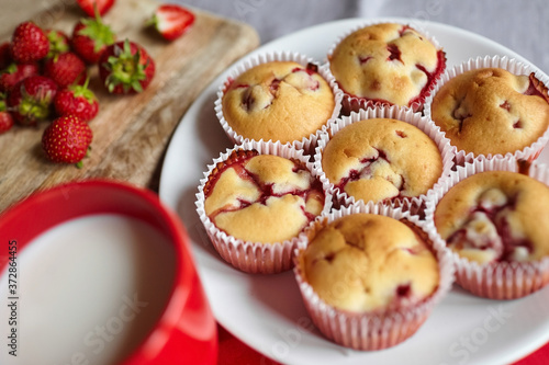 Strawberry muffins on white plate with cup of milk and fresh berries