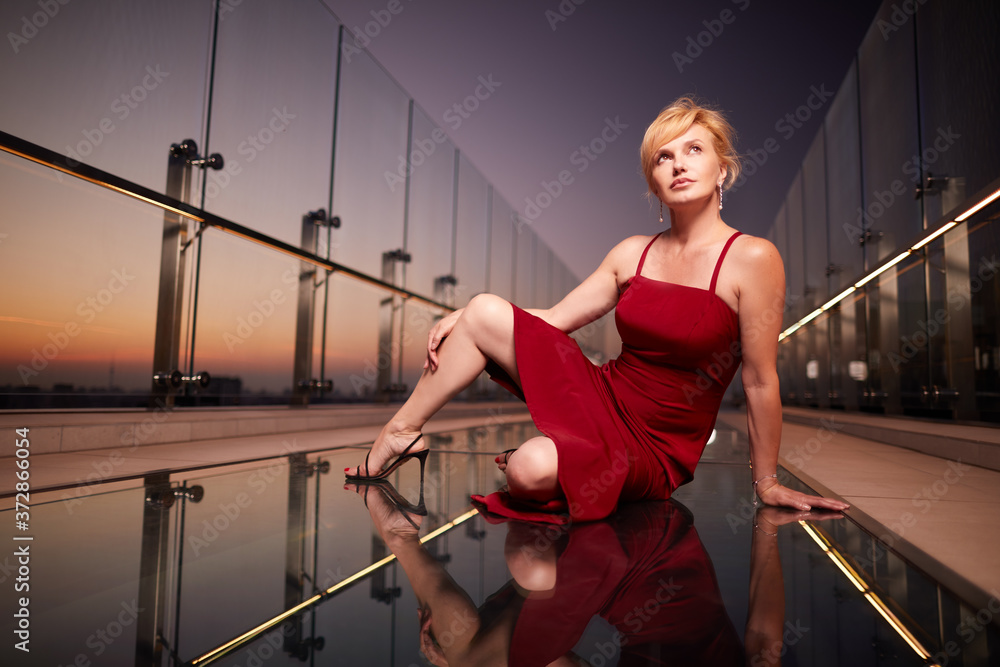 Portrait of beautiful middle age blonde woman in elegant red dress  on rooftop building during sunset