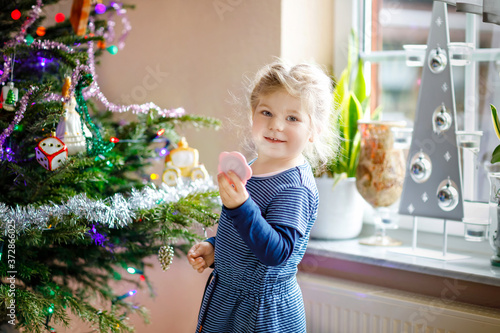 Adorable toddler girl holding little mirror and standing by Christmas tree d. Little child in festive clothes celebration Christmas