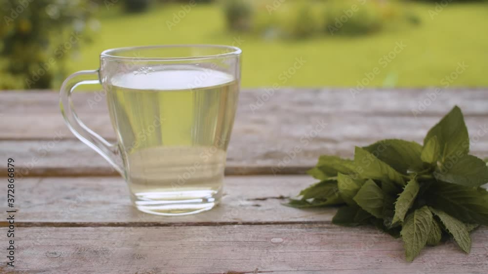 Close-up transparent cup of mint tea on the old wooden table outdoors. A fresh mint on the table. Herbal medicine concept. Dolly shot Close-up transparent cup of mint tea on the old wooden table outdoors. A fresh mint on the table. Herbal medicine concept. Dolly shot
