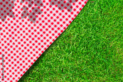 Red checkered table cloth on green turf or grass from top view.