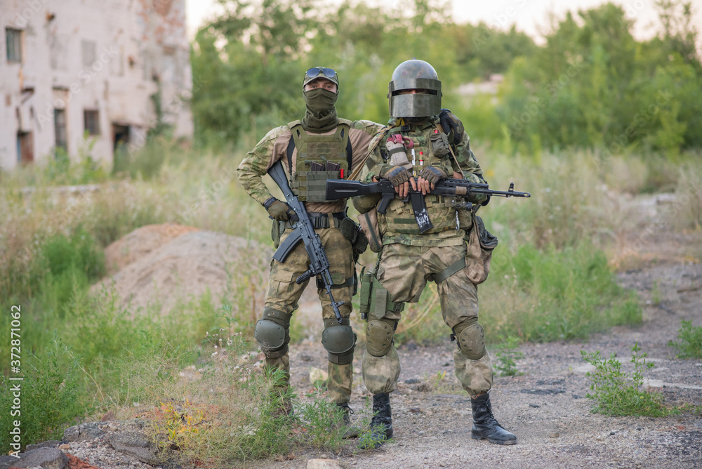 A professional airsoft player stands in a big helmet and a machine gun and with his partner A professional airsoft player stands in a big helmet and a machine gun and with his partner