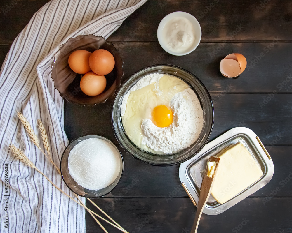 Baking ingredients for shortcrust pastry: butter, flour, eggs, sour cream, a towel on a wooden background. Flatley top view Baking ingredients for shortcrust pastry: butter, flour, eggs, sour cream, a towel on a wooden background. Flatley top view