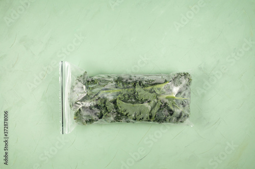 Frozen vegetables. Fresh leaves of kale cabbage in a freezer bag on a green background. Copy space, horizontal orientation photo