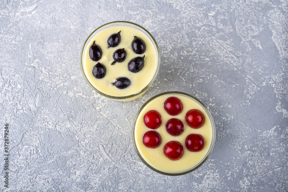Two glass of yellow mango or banana yogurt or smoothie on gray background. Turmeric Lassie (lassi) served with berries. Healthy dairy drink. Copy space for text Two glass of yellow mango or banana yogurt or smoothie on gray background. Turmeric Lassie (lassi) served with berries. Healthy dairy drink. Copy space for text