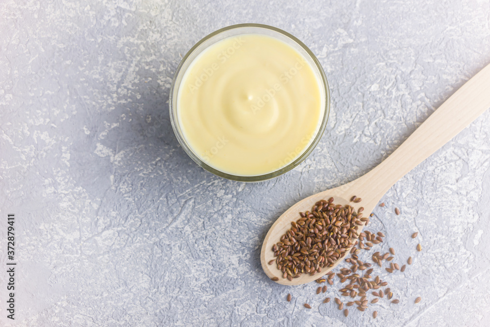 Glass of yellow mango or banana yogurt or smoothie with flax seeds on gray background. Healthy dairy drink. Vegetarian food. Copy space for text Glass of yellow mango or banana yogurt or smoothie with flax seeds on gray background. Healthy dairy drink. Vegetarian food. Copy space for text