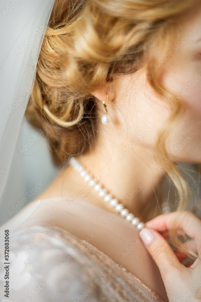 Beautiful caucasian young bride dresses necklace before wedding. Selective focus. Defocus. Blur.