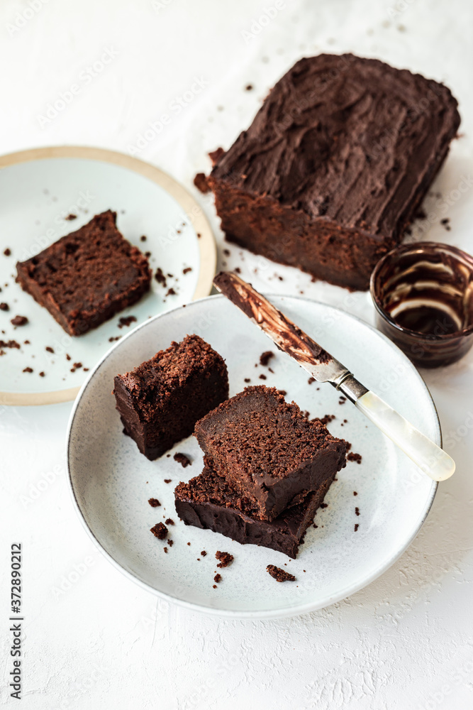 Sliced chocolate loaf cake served on two plates, a knife covered with chocolate, high key, white background Sliced chocolate loaf cake served on two plates, a knife covered with chocolate, high key, white background
