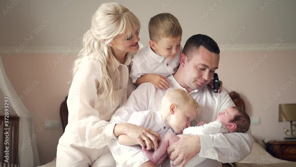 young happy family, father holding a newborn daughter, hugging children and wife. in the bedroom Sitting together two sons boys and little girl. Woman hugs her husband from behind. Great large family young happy family, father holding a newborn daughter, hugging children and wife. in the bedroom Sitting together two sons boys and little girl. Woman hugs her husband from behind. Great large family