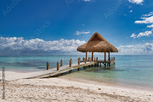 Tropical white sandy beach. Palm leaf roofed wooden pier with gazebo on the beach. Punta Cana, Dominican Republic