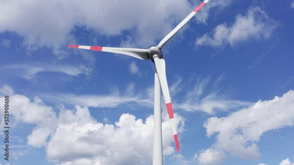 a modern wind wheel spins against a cloudy blue sky filmed downwards in 4k a modern wind wheel spins against a cloudy blue sky filmed downwards in 4k