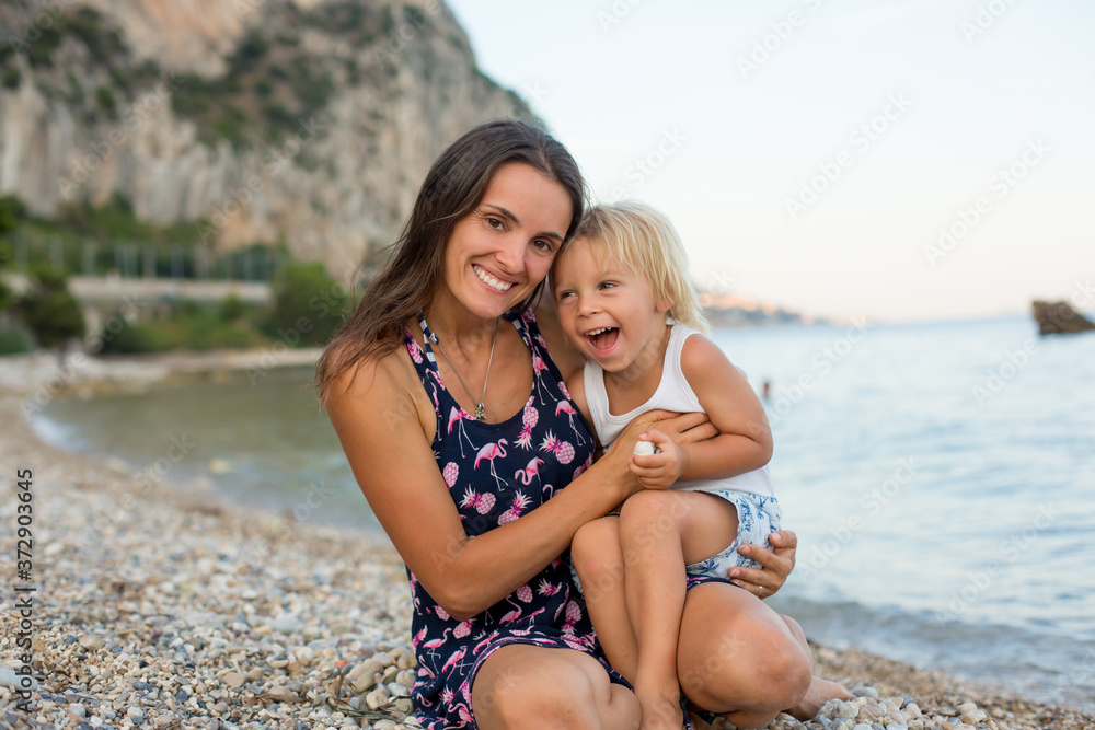 Loving mother and son, blond toddler boy, hugging at the beach, enjoying time