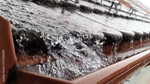 Close up of water falling down to gutter from the roof during heavy rain storm, slow motion footage clip.