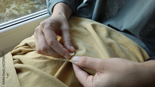 Woman's hands getting ready to sew button to yellow shirt. Female at work