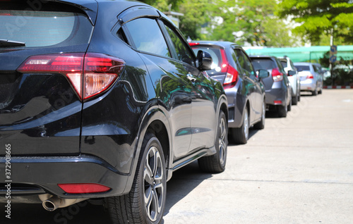Closeup of rear, back side of black car with other cars parking in outdoor parking area with natural background in sunny day. 