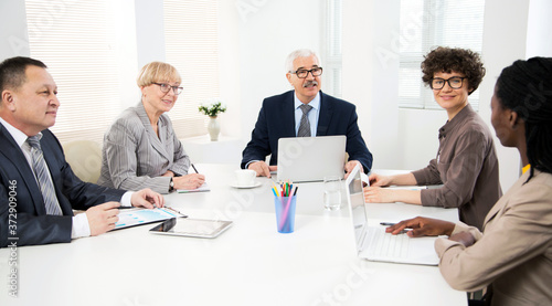 International group of business people working and communicating sitting near office desk.