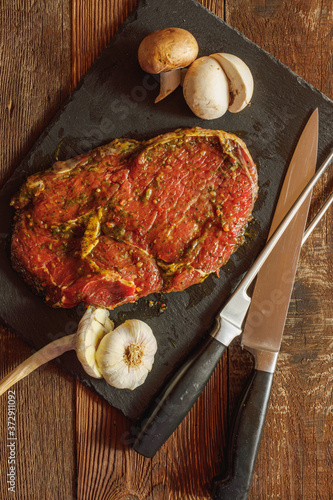 Slice of spiced raw beef with garlic and mushroom on slate plate with meat knife and fork on wooden table