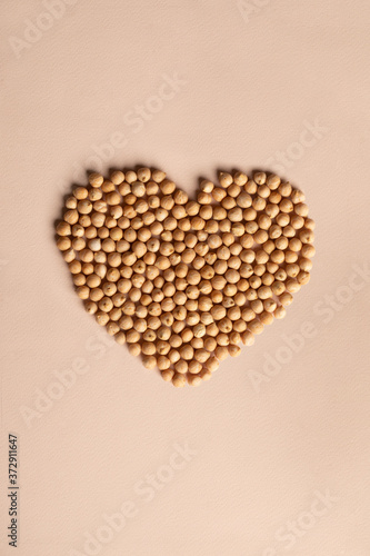 Pile of kabuli chickpeas in shape of heart on beige, light tan background. Heap of legumes bean seeds grains, top view. Ingridient for hummus, falafel. East Asian traditional cuisines. Healthy food.