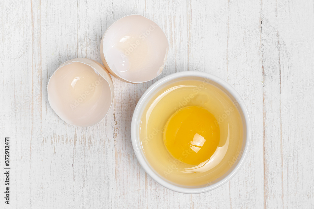 Row fresh egg in ceramic small white plate and two parts of shell above view on painted wooden background macro Row fresh egg in ceramic small white plate and two parts of shell above view on painted wooden background macro