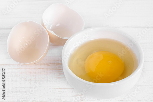 Row fresh egg in ceramic small white plate and two parts of shell full view on painted wooden background macro