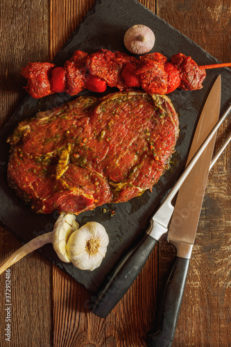 Slice of spiced beef with bbq skewer of beef and tomato with garlic knife and fork on slate plate on wooden table