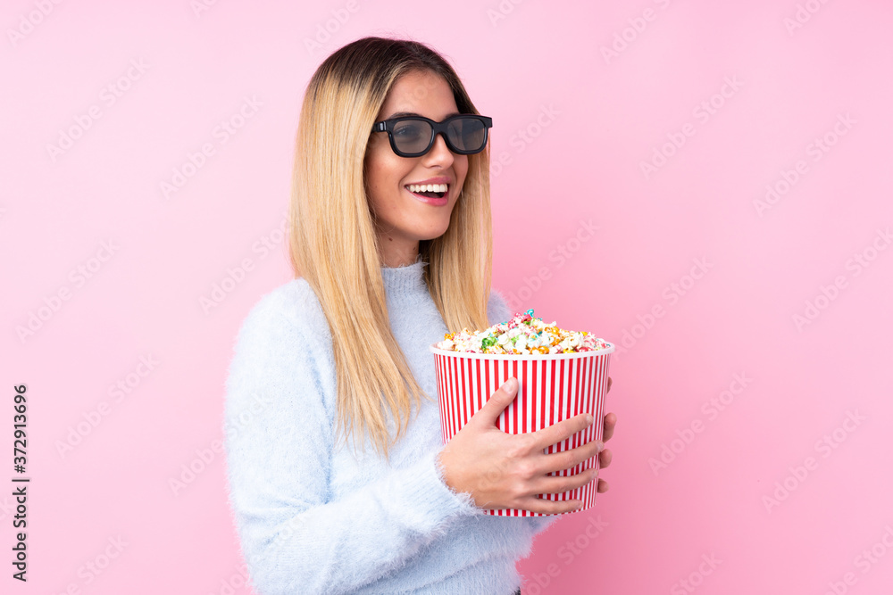 Young Uruguayan woman over isolated pink background with 3d glasses and holding a big bucket of popcorns Young Uruguayan woman over isolated pink background with 3d glasses and holding a big bucket of popcorns