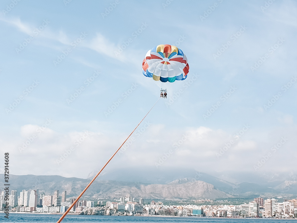 People paragliding in Benidorm Spain in the blue sky with the summer sun behind a speedboat and the city coastline in the distance People paragliding in Benidorm Spain in the blue sky with the summer sun behind a speedboat and the city coastline in the distance