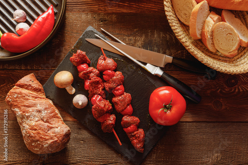 bbq skewer of beef and tomato on slate plate with garlic and mushroom bread in basket chilli pepper and cast-iron grill pan