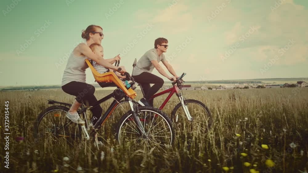 Family cycling outdoor. Young family cycling with baby on a green summer field. Family cycling outdoor. Young family cycling with baby on a green summer field.