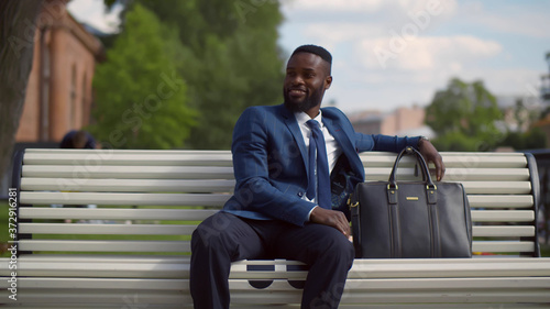 Portrait of young attractive african businessman relaxing sitting on bench outdoors