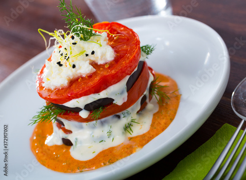 Grilled eggplant and tomatoes stack seasoned with spicy cream-tomato sauce served on white plate