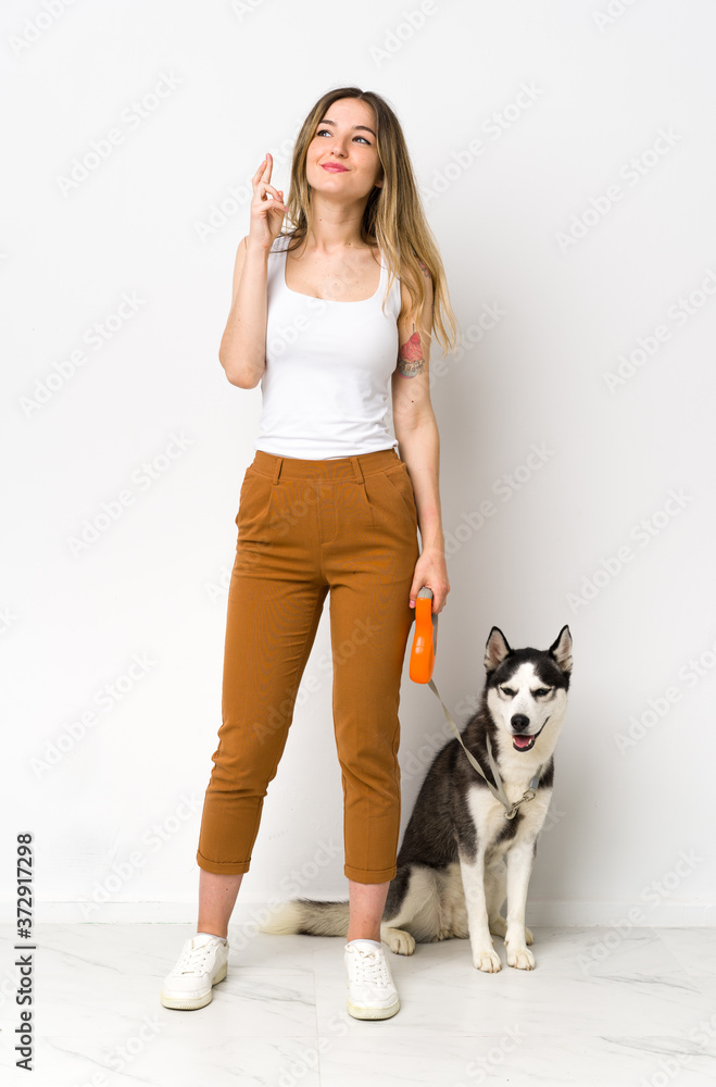 A full length young pretty woman with her dog with fingers crossing and wishing the best