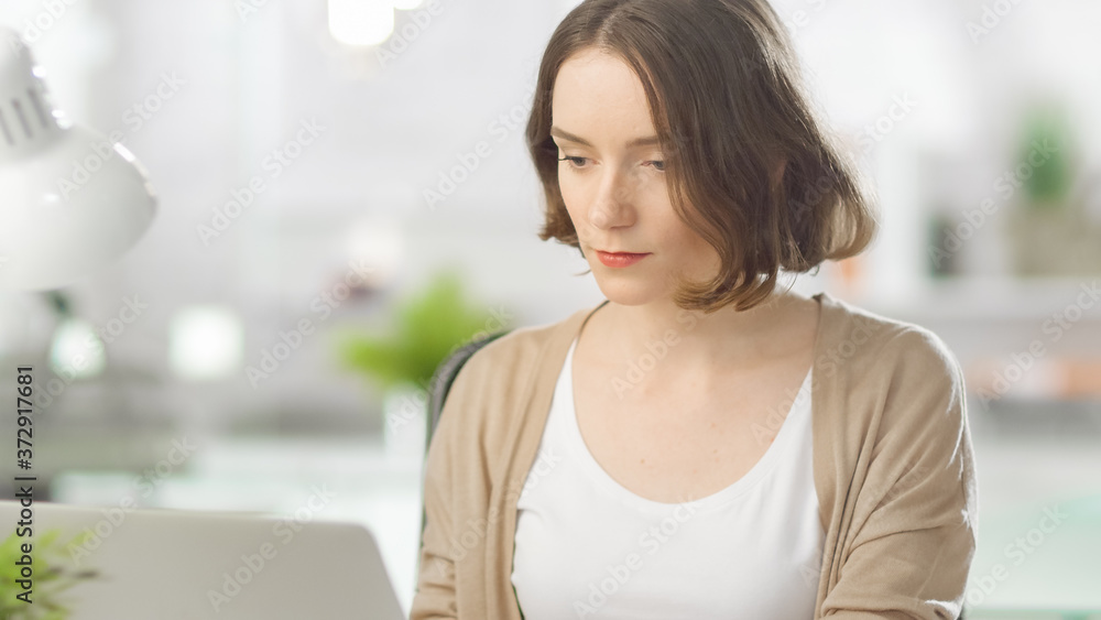 Shot of Focused Young Woman Working on Her Laptop Computer. In the Background Blurred Bright Modern Loft Office.