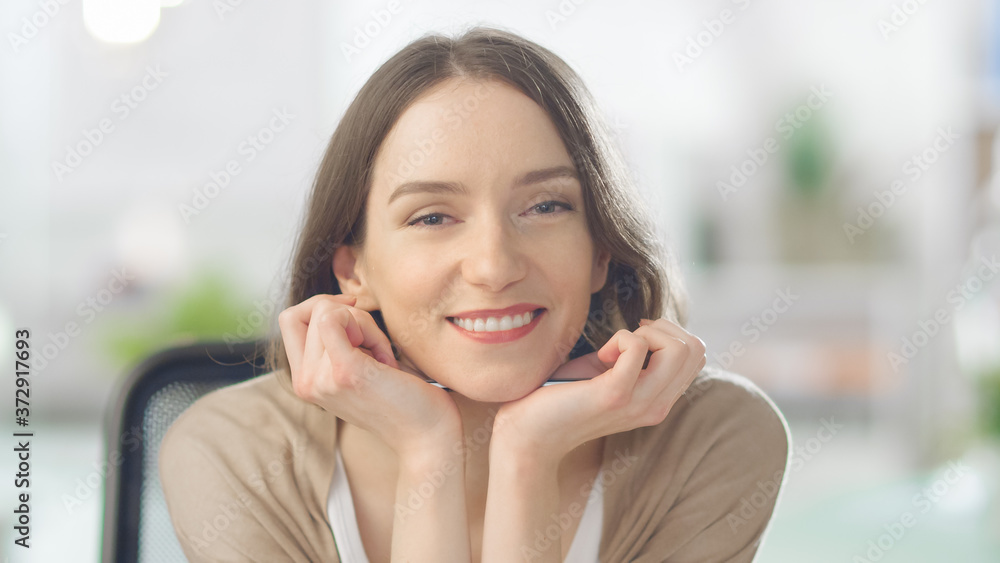 Creative Young Woman Charmingly Smiles at the Camera. She is Working in a Blurred Bright Modern Loft Office. Creative Young Woman Charmingly Smiles at the Camera. She is Working in a Blurred Bright Modern Loft Office.