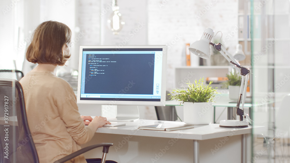 Young Creative Woman Software Developer Writes Code on Her Desktop Computer. She Sits in Her Bright Modern Developers Office. Young Creative Woman Software Developer Writes Code on Her Desktop Computer. She Sits in Her Bright Modern Developers Office.