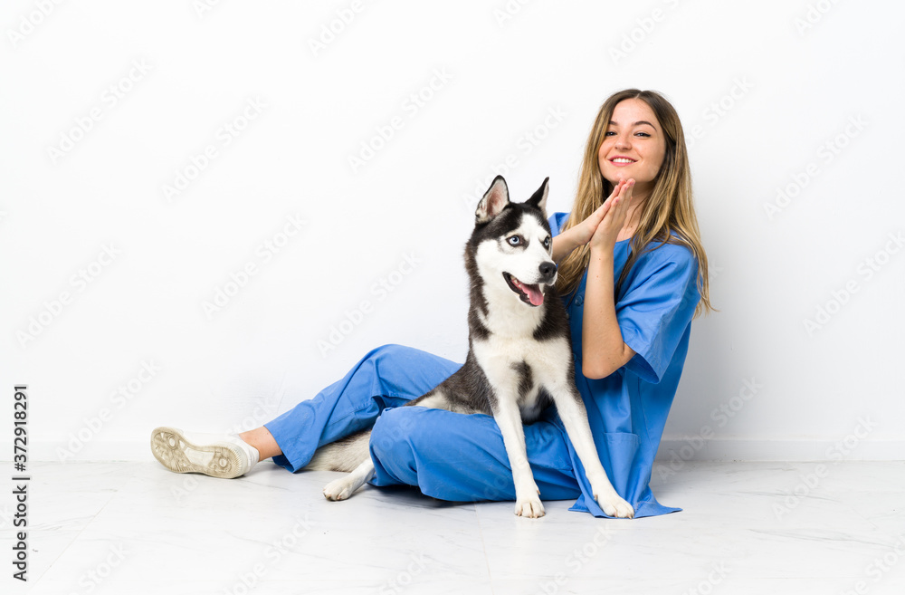 Veterinary doctor with Siberian Husky dog sitting on the floor applauding Veterinary doctor with Siberian Husky dog sitting on the floor applauding