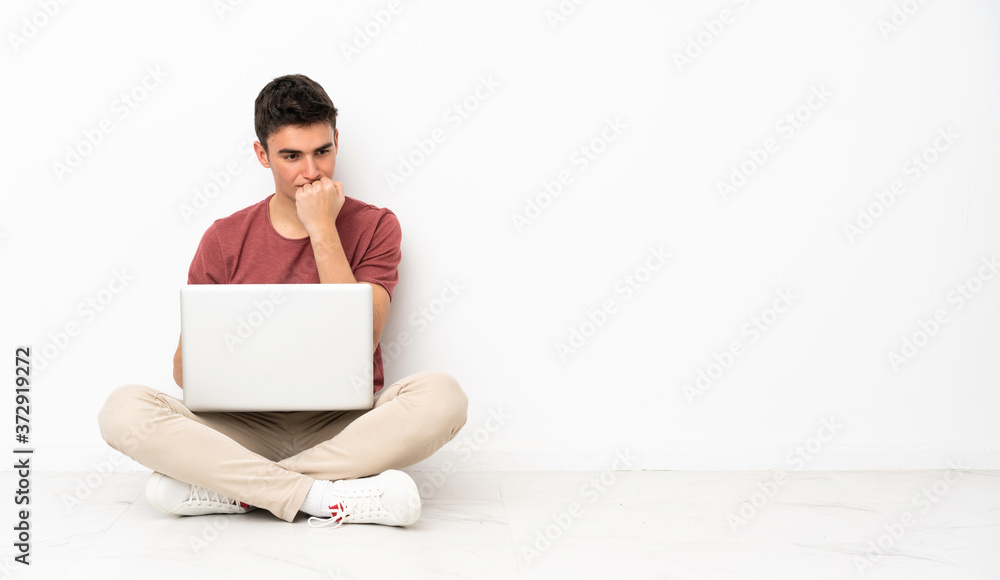 Teenager man sitting on the flor with his laptop having doubts