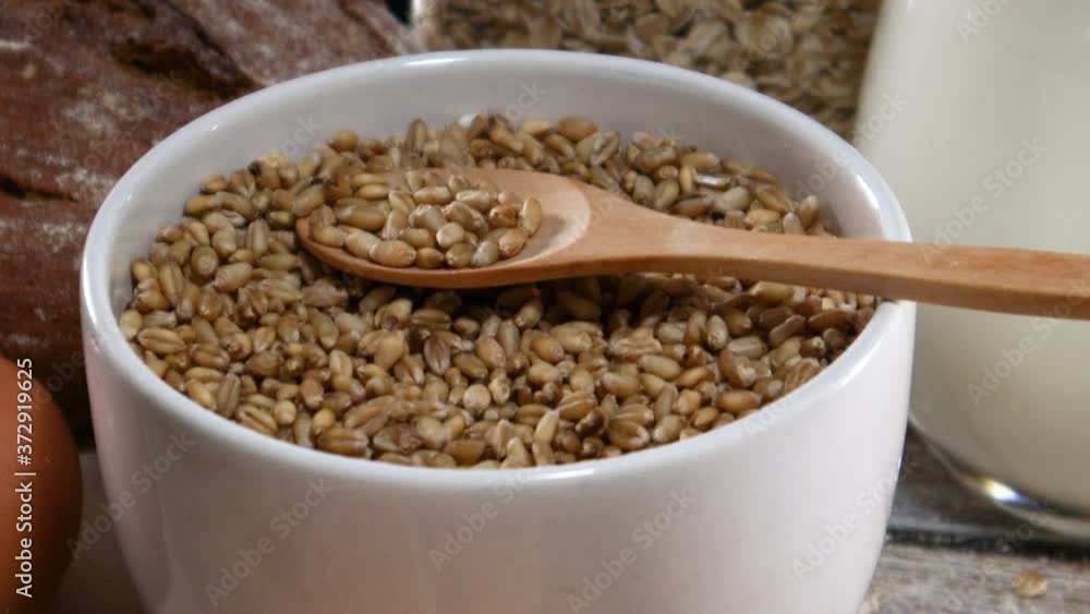 Close up of organic grain in white bowl with wooden spoon and baking groceries on the table Close up of organic grain in white bowl with wooden spoon and baking groceries on the table