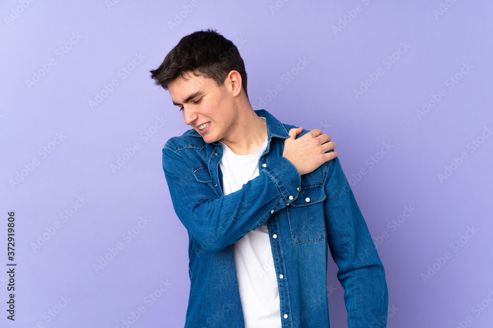 Teenager caucasian handsome man isolated on purple background suffering from pain in shoulder for having made an effort Teenager caucasian handsome man isolated on purple background suffering from pain in shoulder for having made an effort