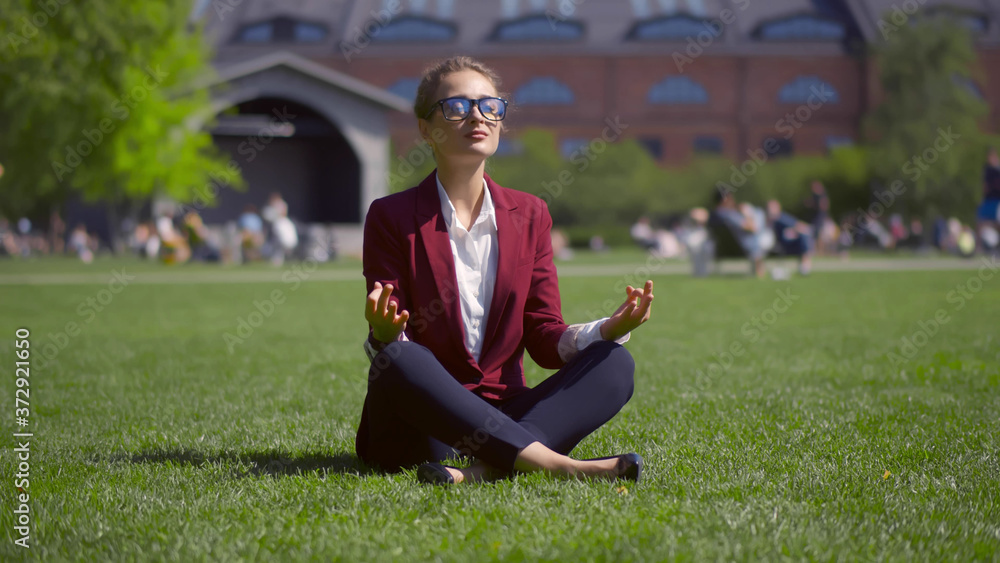 Fototapeta premium Beautiful businesswoman calming and meditating on grass in summer park