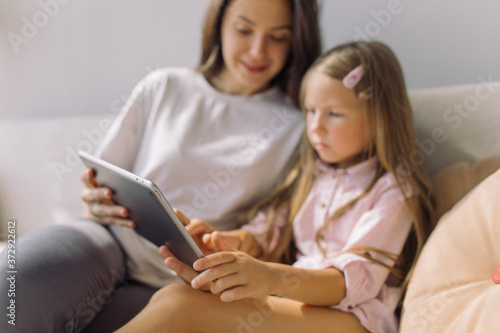 Nanny showing educational cartoon on tablet to little girl. Focus on technology.