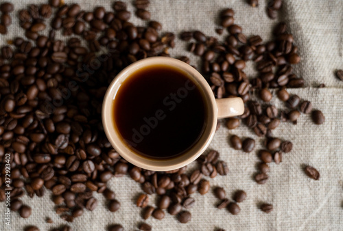 Coffee cup with roasted coffee beans on linen background. Mug of black coffe with scattered coffee beans. Fresh coffee beans.