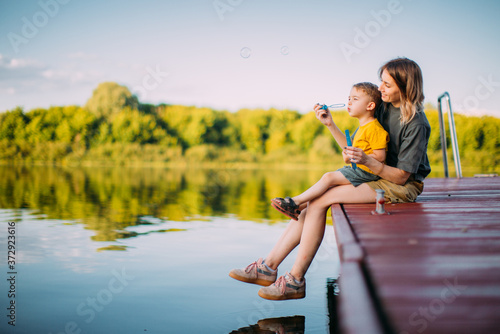 Fototapete Cool mother and baby boy sitting on dock launch soap bubbles