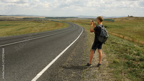 A young man takes pictures on a phone landscape next to a country road