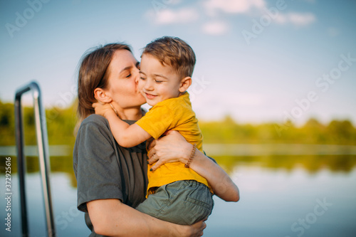 Mother kiss and hug son on dock on nature background. Summer photography for blog or advertising about family and travel