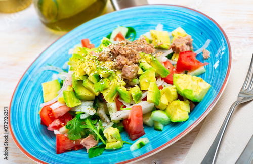 Delicious salad with canned tuna, fresh tomatoes, avocado, onion, corn and greens served on blue plate