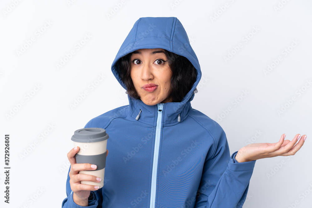 Mixed race woman wearing winter clothes with the hood on and holding a hot takeaway coffee over isolated white background making doubts gesture while lifting the shoulders Mixed race woman wearing winter clothes with the hood on and holding a hot takeaway coffee over isolated white background making doubts gesture while lifting the shoulders