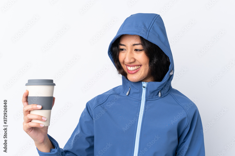 Mixed race woman wearing winter clothes with the hood on and holding a hot takeaway coffee over isolated white background with happy expression Mixed race woman wearing winter clothes with the hood on and holding a hot takeaway coffee over isolated white background with happy expression