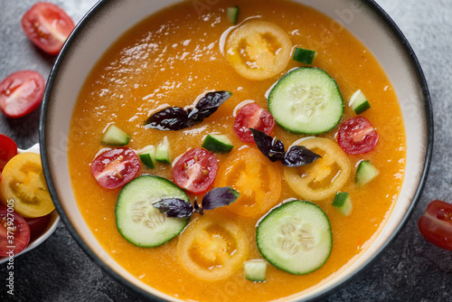 Close-up of yellow cold soup gazpacho topped with cucumber and tomato slices, elevated view, horizontal shot, selective focus